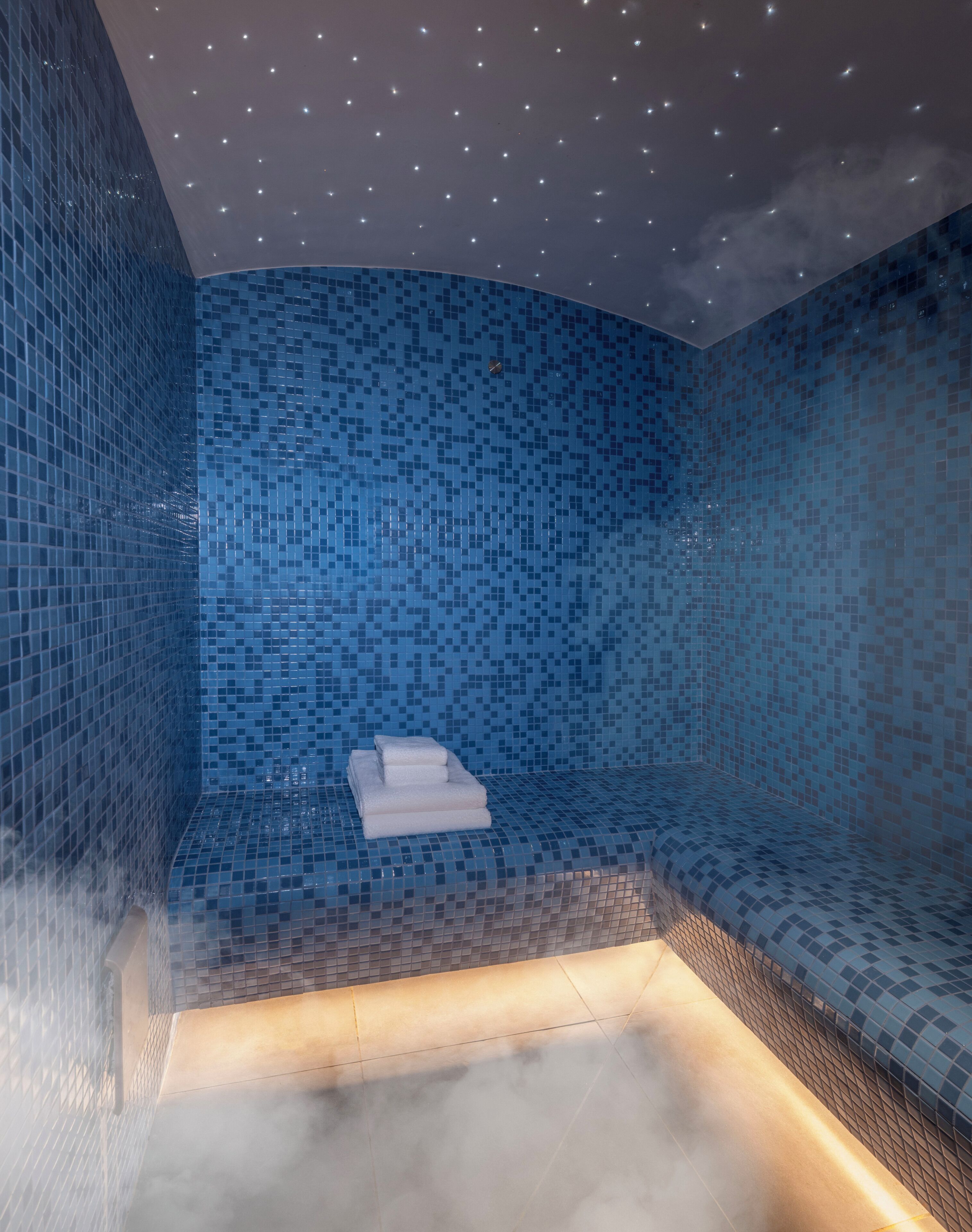 Un baño moderno con mosaicos azules, una bañera integrada y un perchero.