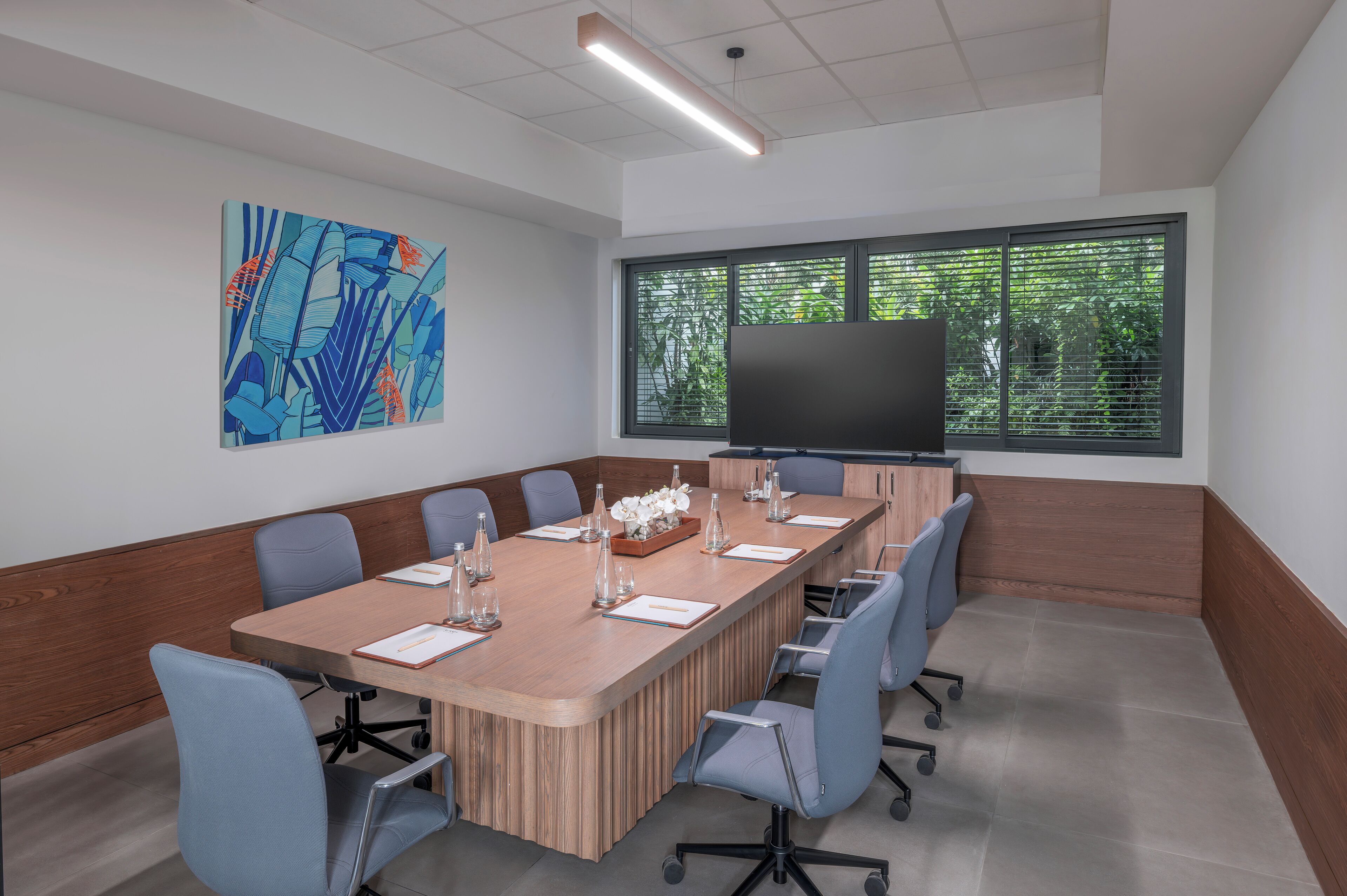 A conference room with a long table, chairs, a flat-screen TV, and a large abstract painting on the wall.