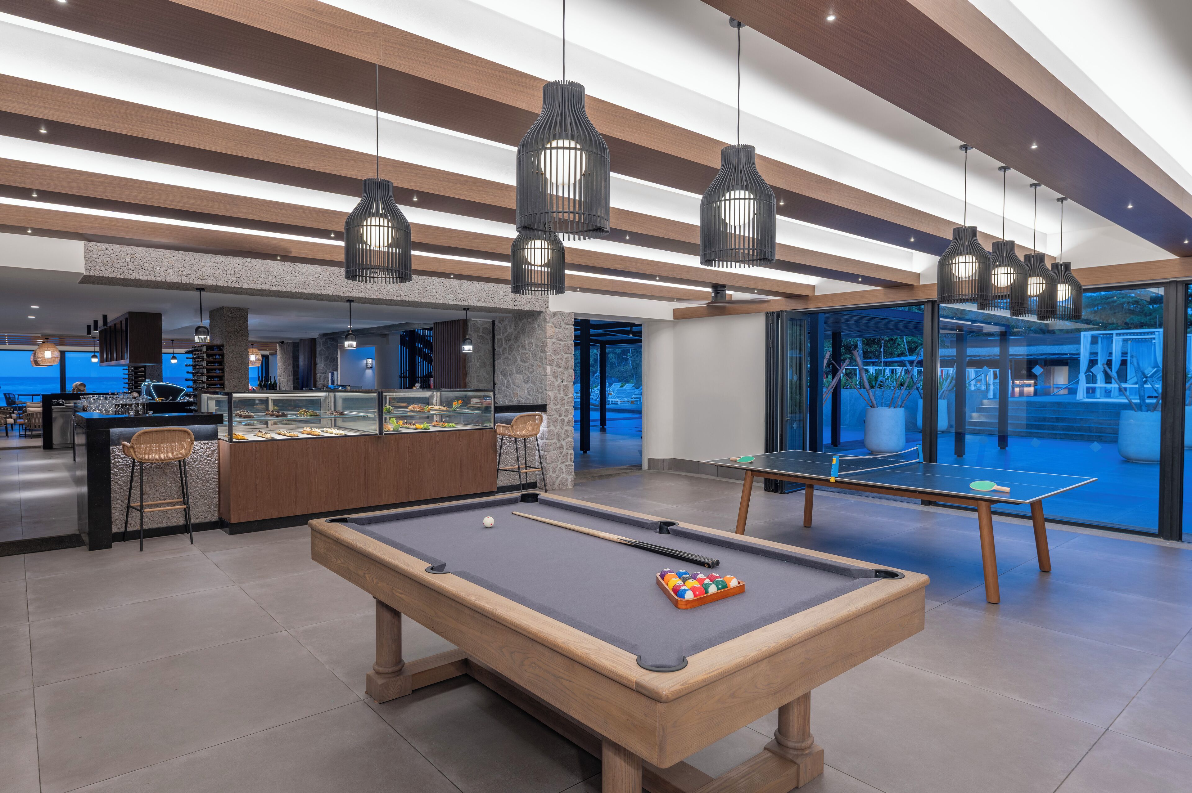 A pool table with a cue stick and a set of billiard balls in a modern indoor setting with wooden beams and pendant lighting.