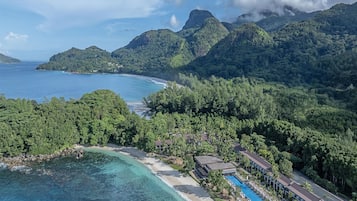 A resort with a swimming pool, beach, and mountainous backdrop.