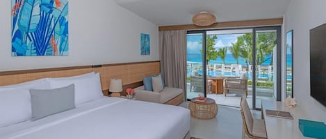 A hotel room with a large bed, a desk, a chair, a small table, and a view of the pool and ocean.