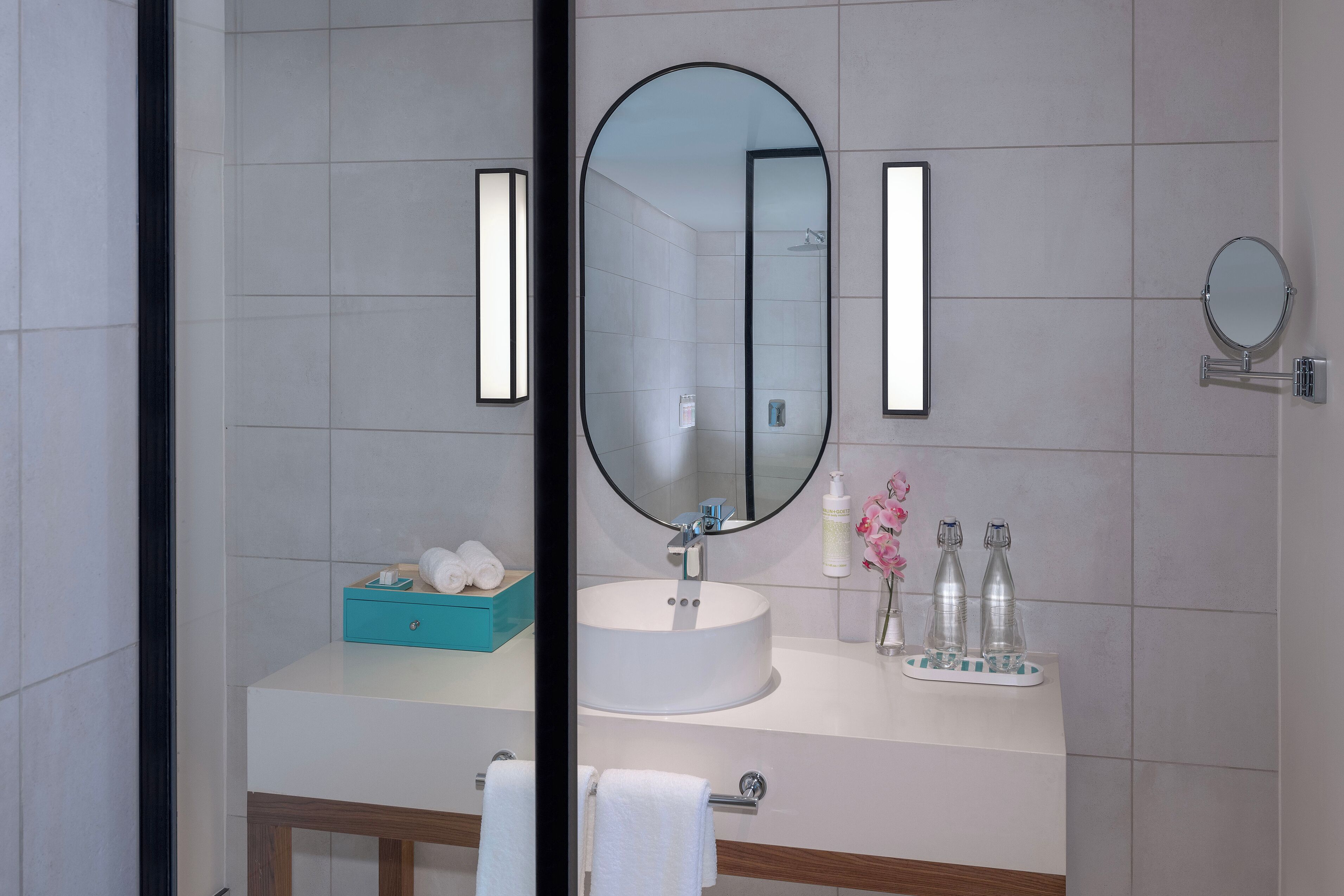 A modern bathroom with a large oval mirror, a white sink, and a blue towel holder.