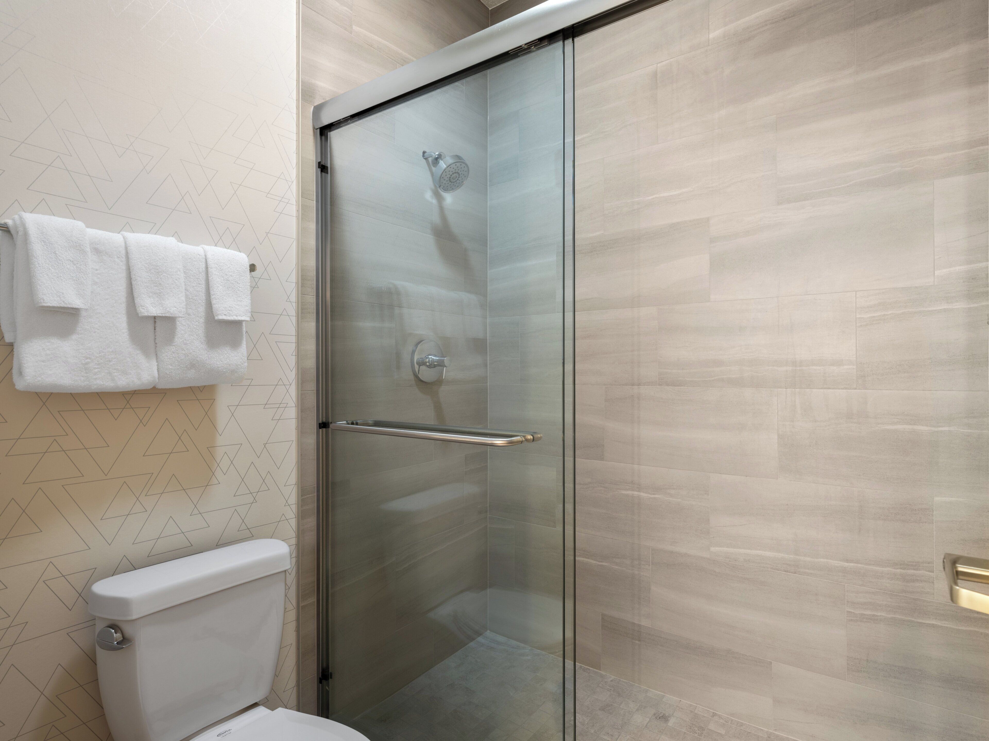 Un baño moderno con cabina de ducha de vidrio, inodoro y toallero con toallas dobladas.