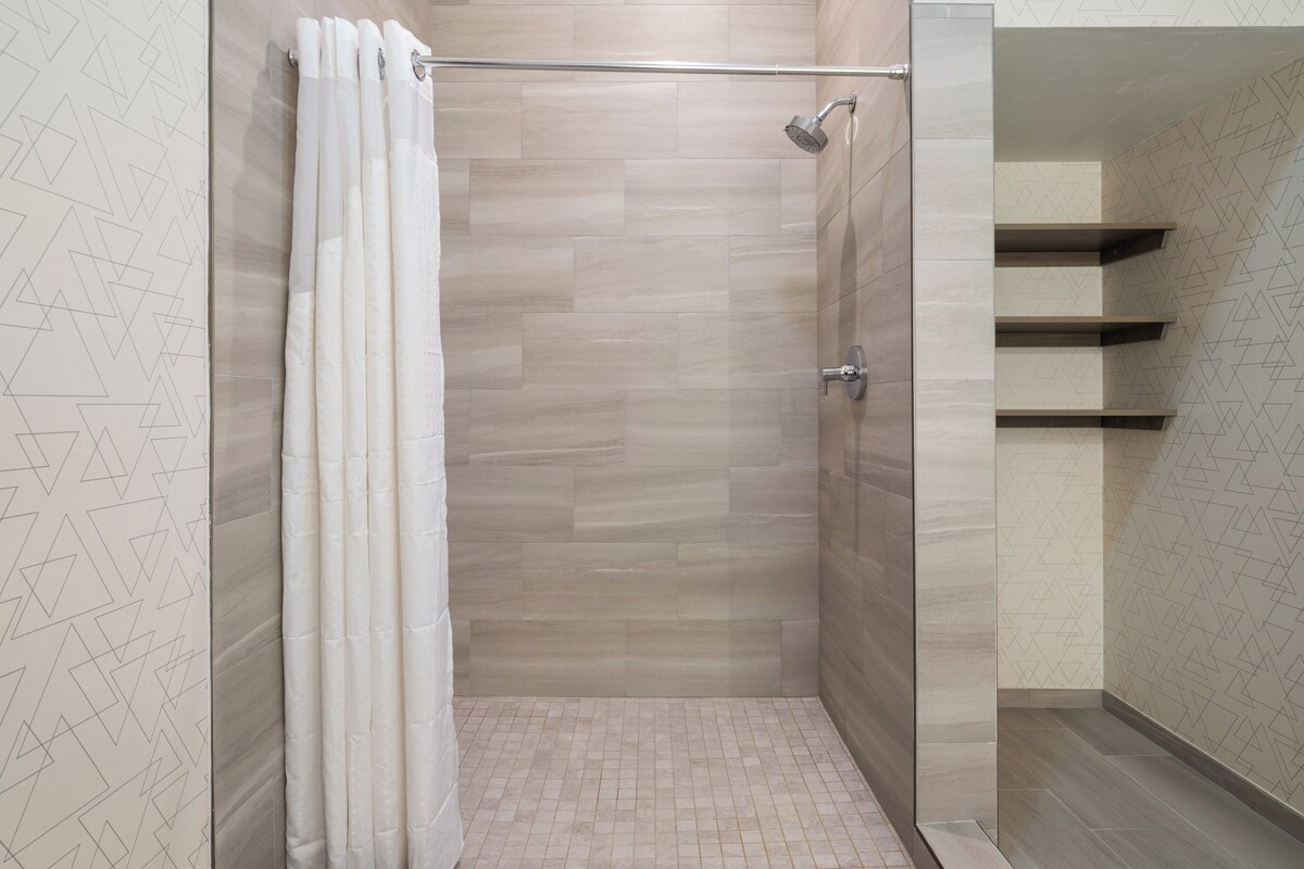 A modern shower area with a glass door, a showerhead, and a tiled floor.