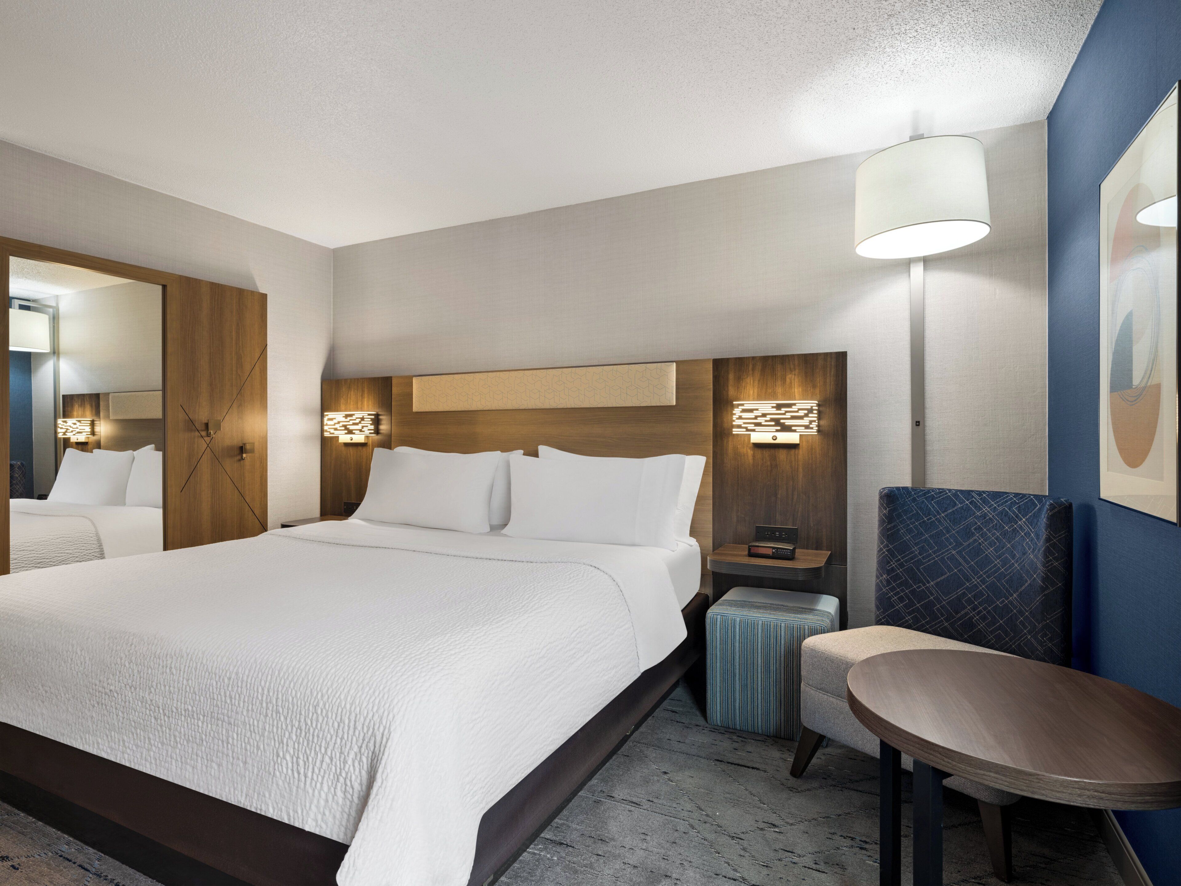 A hotel room with a large bed, bedside tables, a lamp, a chair, and a mirror.