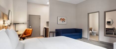 Una habitación de hotel moderna con una cama grande, un sofá azul, un escritorio y una silla.