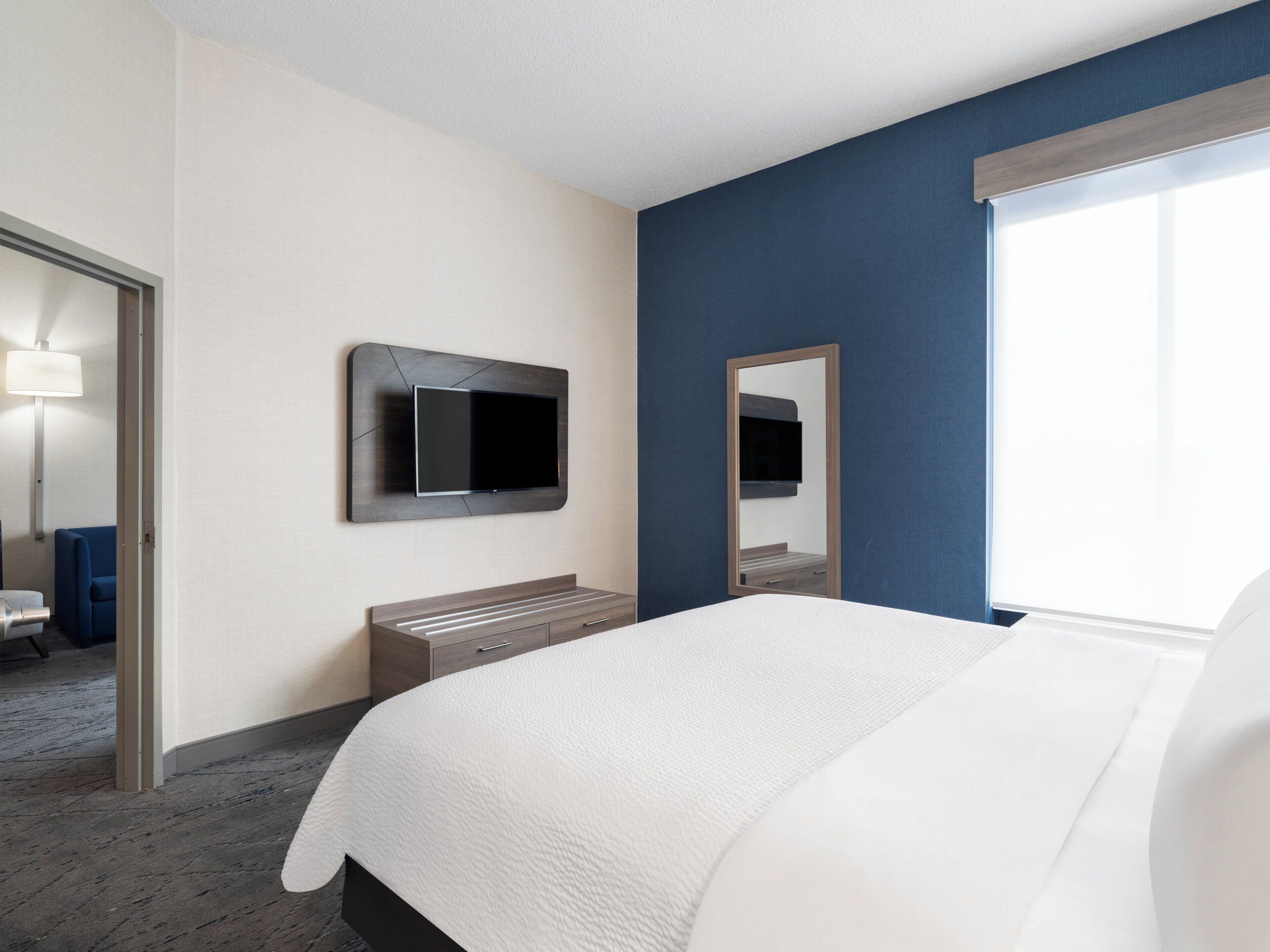 Una habitación de hotel con cama, televisión montada en la pared, mesita de noche y ventana.