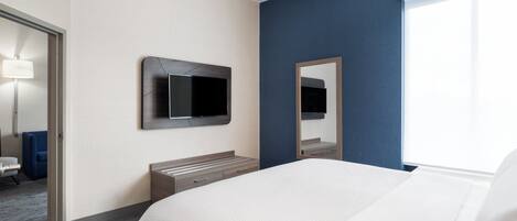 Una habitación de hotel con cama, televisión montada en la pared, mesita de noche y ventana.