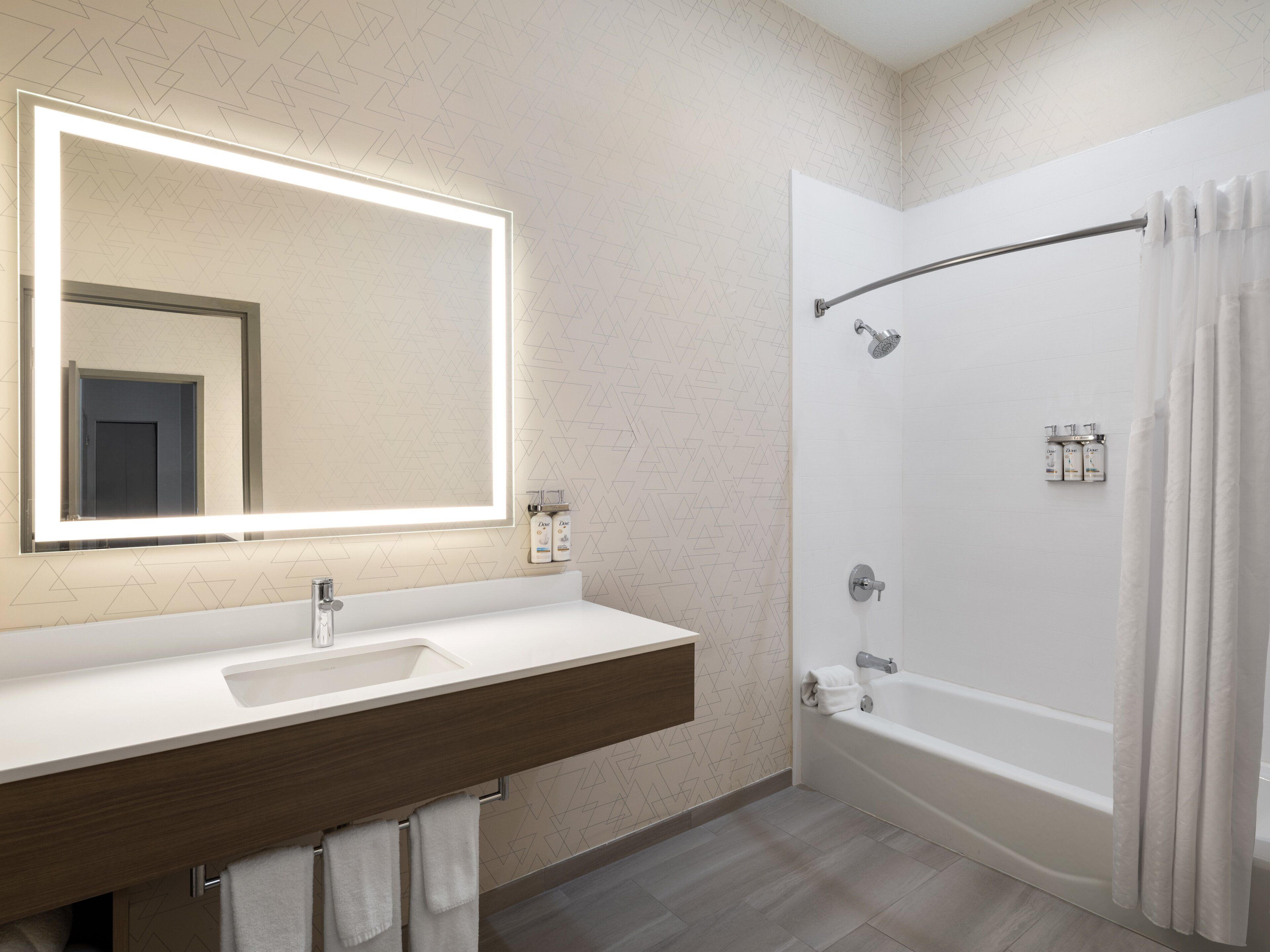 Un baño moderno con un espejo grande, un lavamanos, una bañera y una ducha.