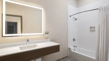 Un baño moderno con un espejo grande, un lavamanos, una bañera y una ducha.
