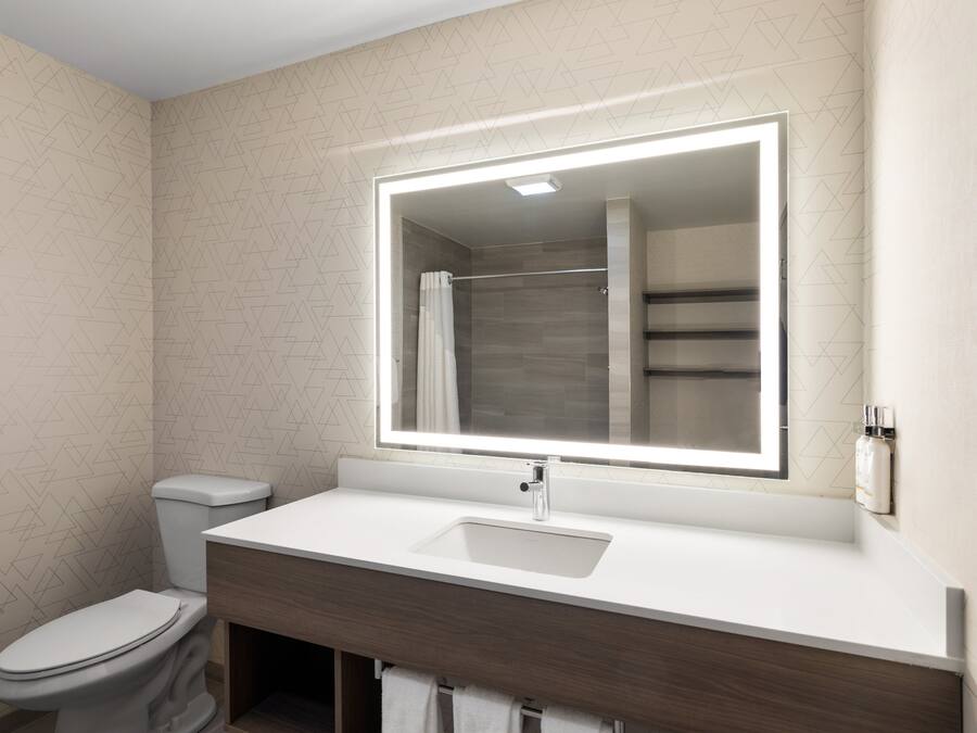A modern bathroom with a large mirror, white sink, and toilet.