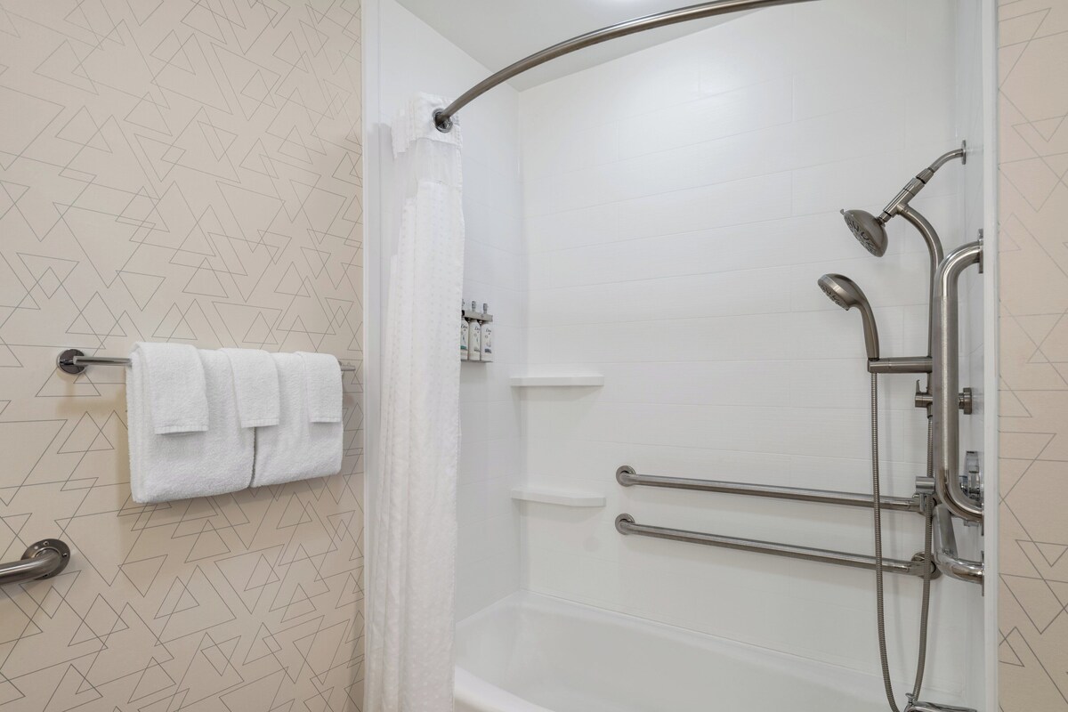 A modern bathroom with a shower, grab bars, and a towel rack.
