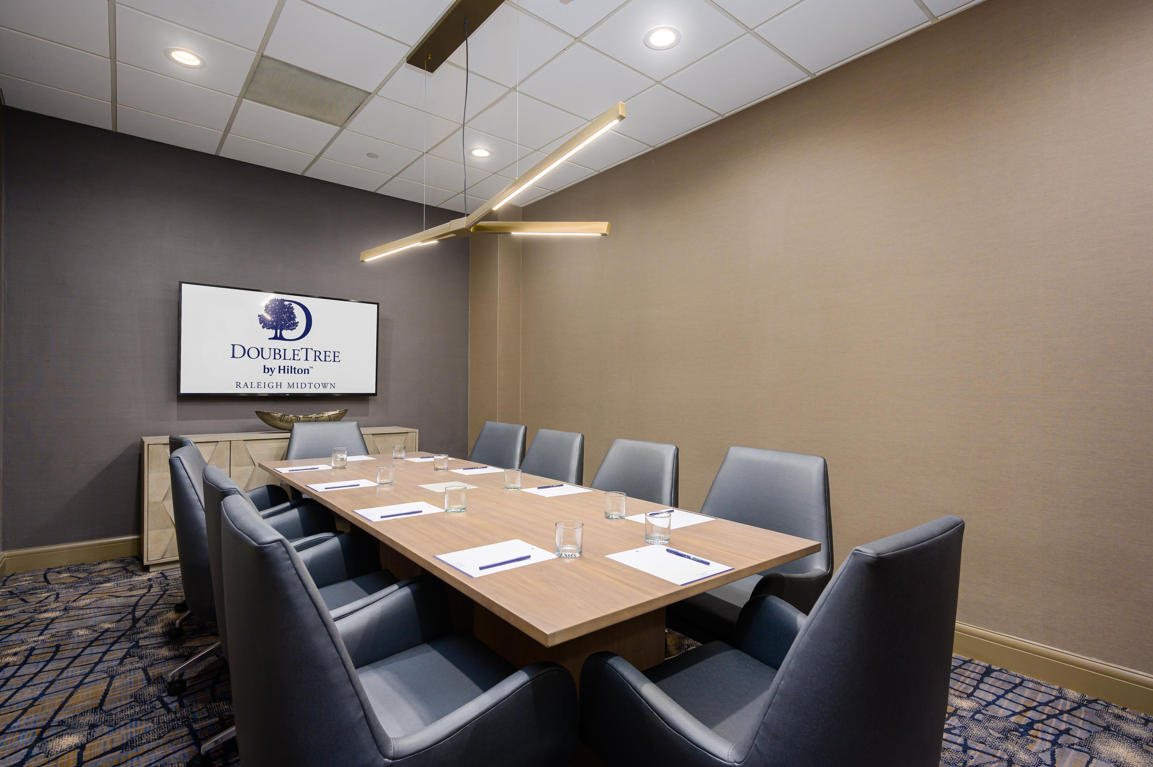 Una sala de conferencias con una larga mesa, sillas, una pantalla de proyector e iluminación empotrada en el techo.