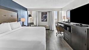 A hotel room with a large bed, a desk with a flat-screen TV, a chair, a desk lamp, and a large window. - DoubleTree by Hilton Raleigh Midtown, NC (Raleigh)
