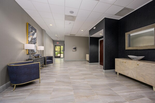 A spacious lobby with a marble floor, a blue sofa, a cabinet with a bowl, and a large mirror.