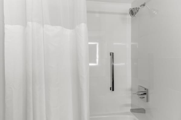 Une salle de bain moderne dotée d’une cabine de douche en verre, d’un pommeau de douche apparent et d’une poignée métallique.