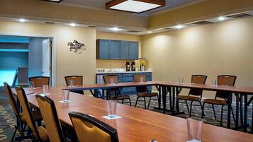 Uma sala de conferências com uma mesa comprida, cadeiras e uma copa ao fundo.