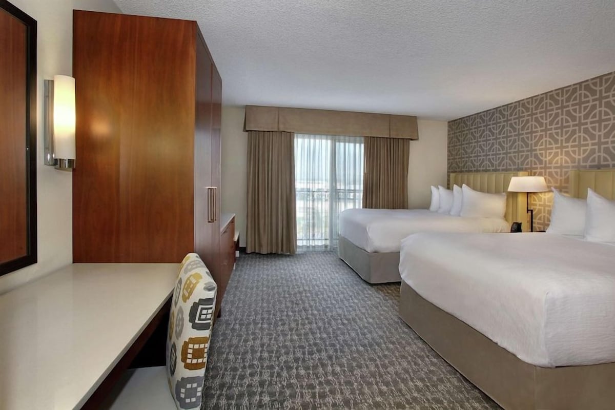 A hotel room with two beds, a desk, a wardrobe, and a patterned wall.
