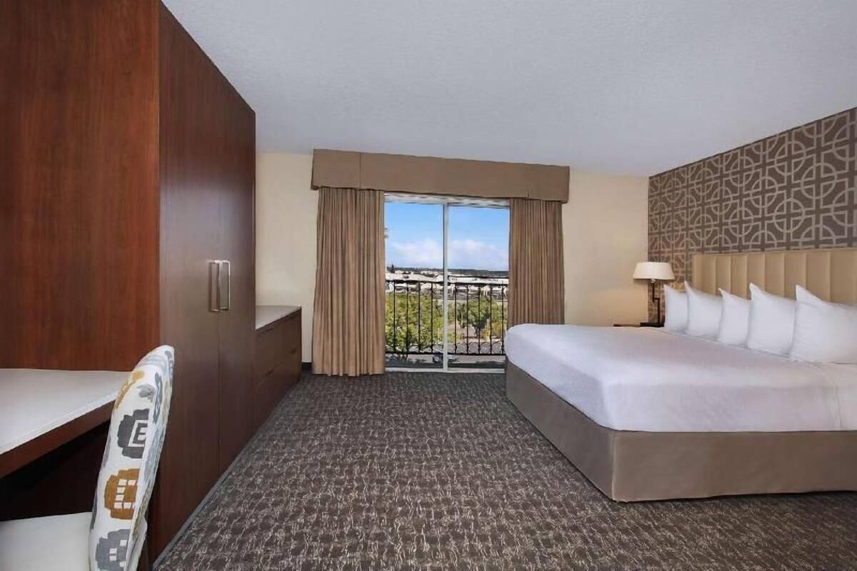 A hotel room with a bed, a desk, a chair, a window with curtains, and a view of the city.
