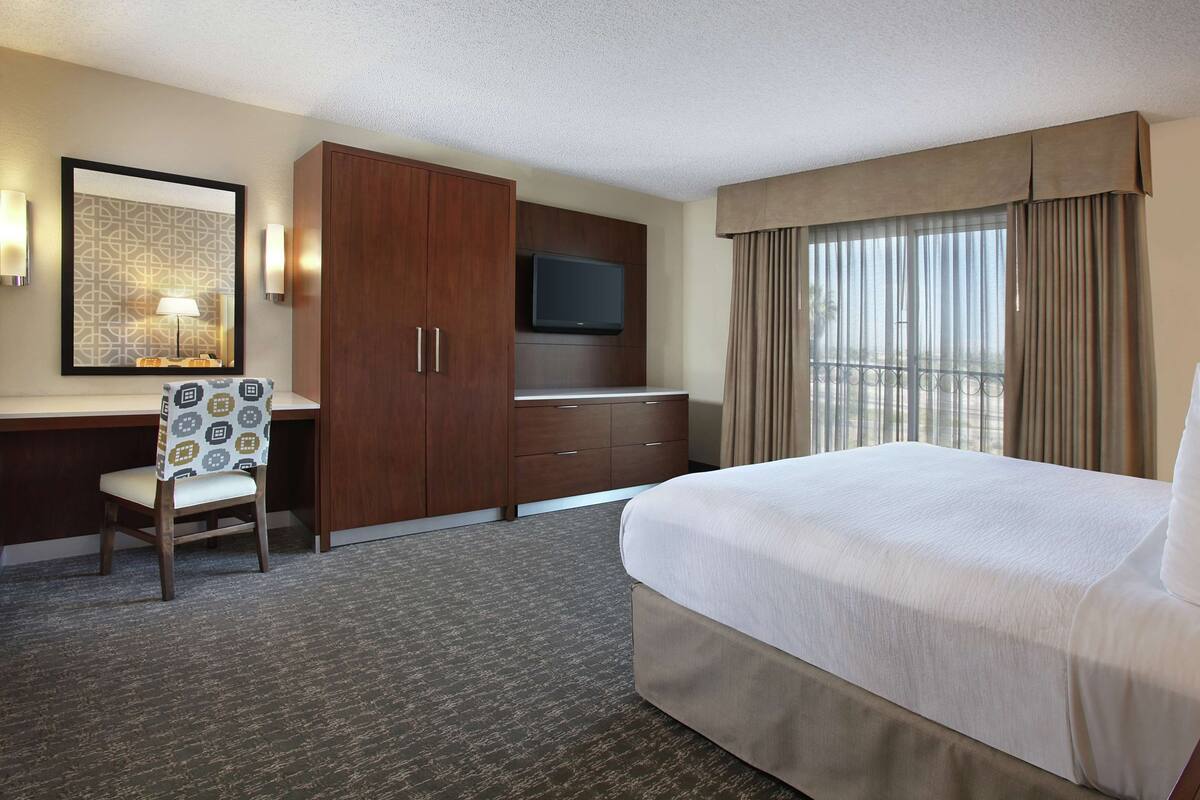 A hotel room with a large bed, a desk with a chair, a television, and a window with curtains.