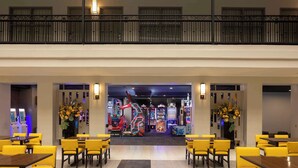 A hotel lobby with yellow chairs and tables, a balcony with a railing, and arcade games in the background. - Embassy Suites by Hilton Anaheim North (Anaheim)