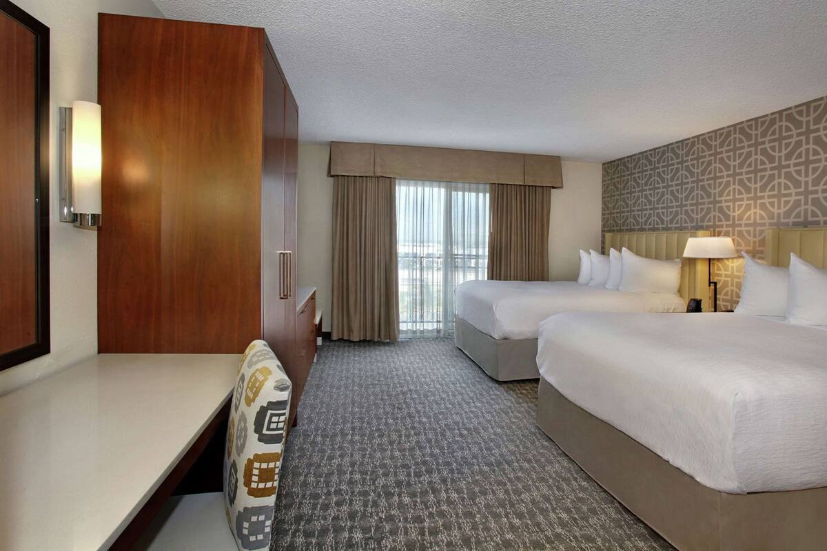 A hotel room with two beds, a desk, a wardrobe, and a patterned wall.