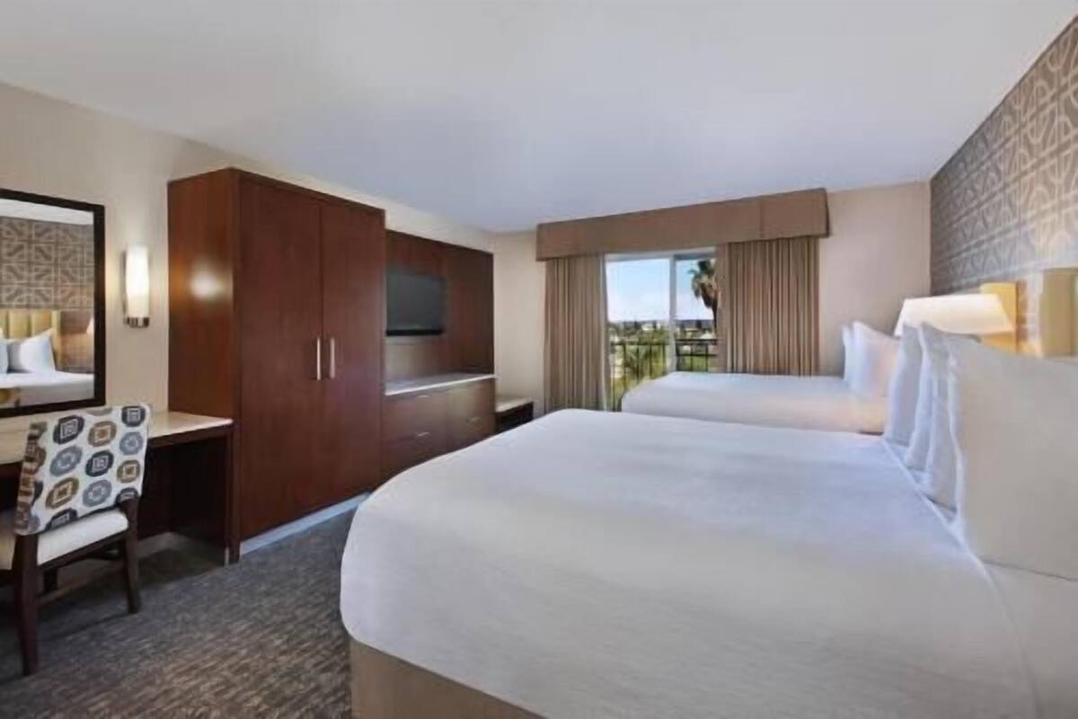 A hotel room with two beds, a TV, a desk, and a large window with a view.