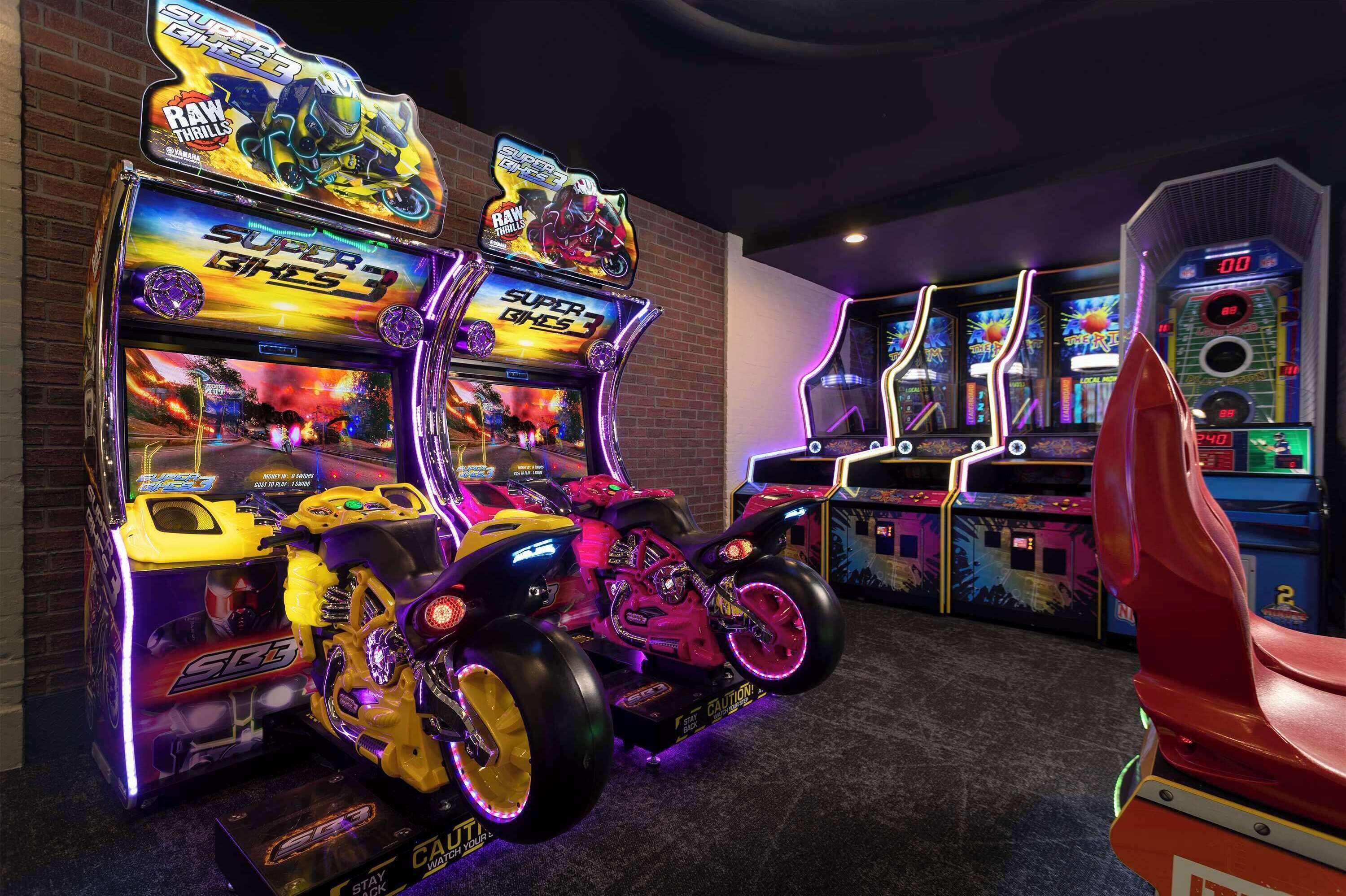 An arcade with various gaming machines, including a motorcycle-themed game.