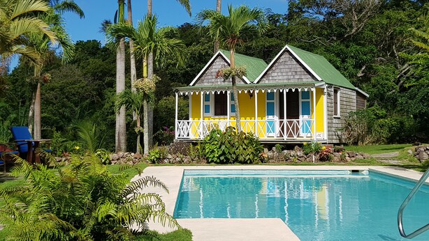 A two-story house with a green roof and a balcony, surrounded by lush greenery and a swimming pool. - Hermitage Nevis (Charlestown)