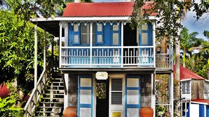 A two-story house with a red roof, blue and white exterior, and a balcony. - Hermitage Nevis (Charlestown)