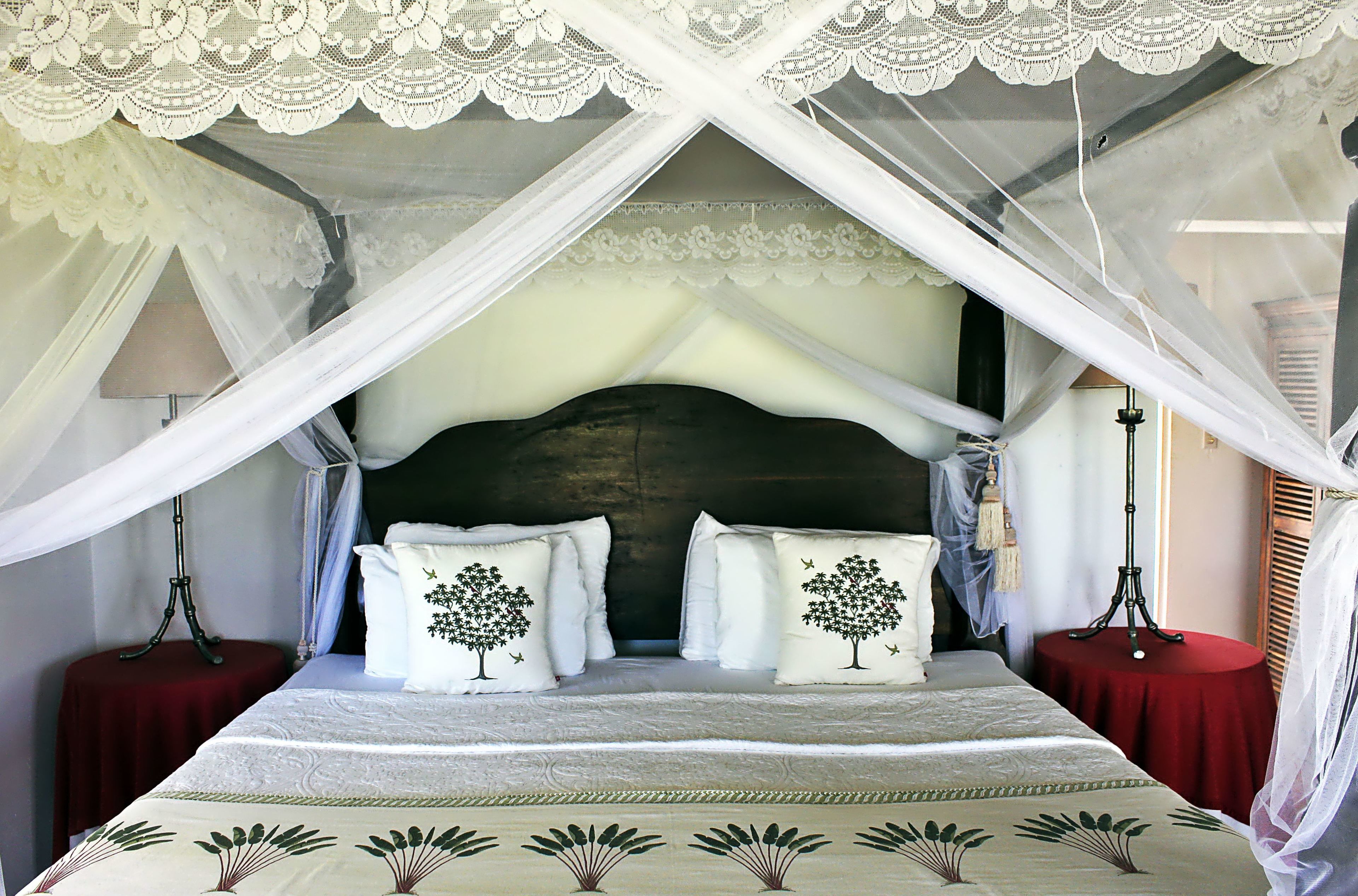A bed with a canopy, two pillows with tree designs, a red table beside the bed, and a lamp on the table.