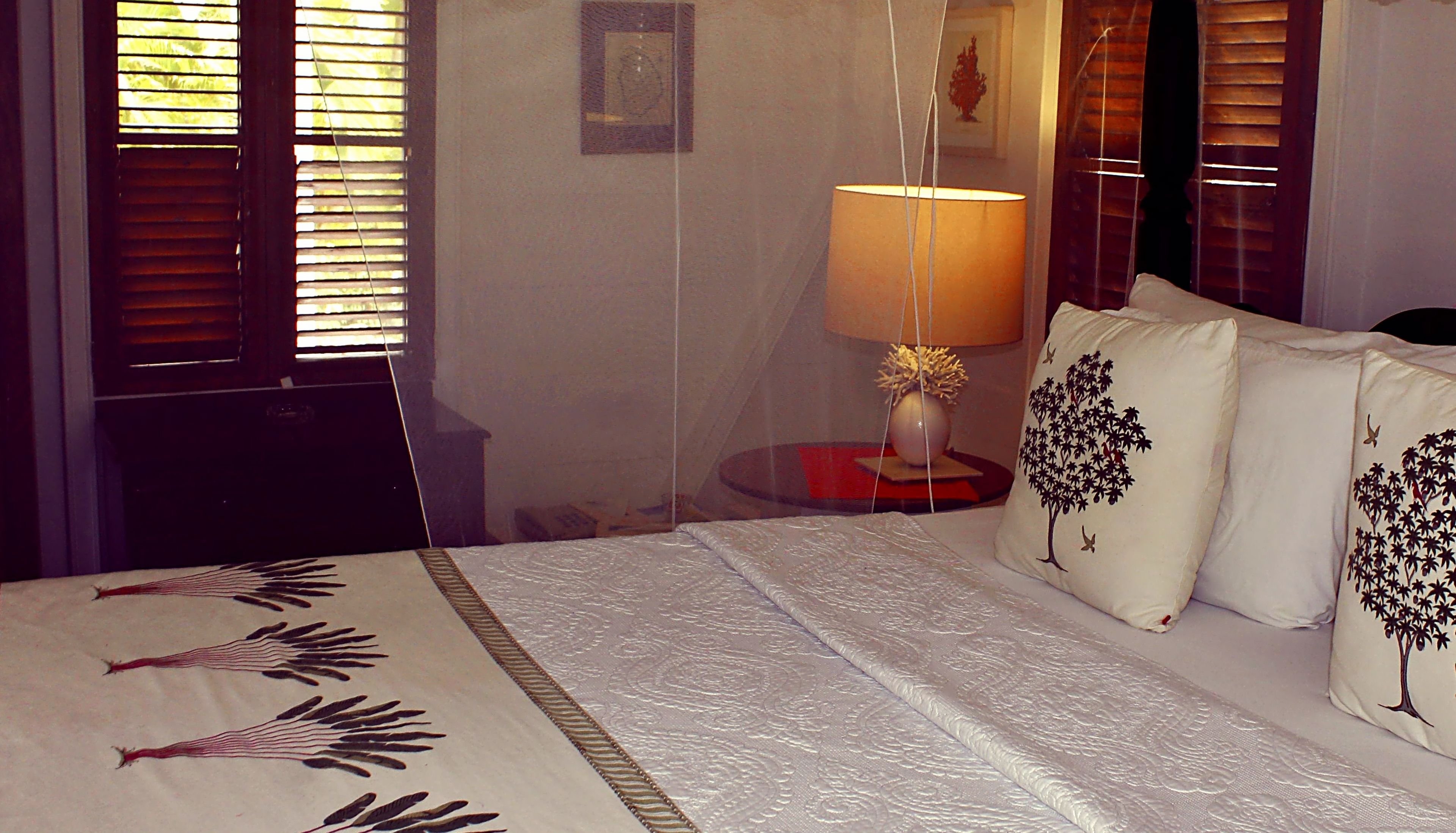 A hotel room with a bed, a bedside lamp, and a nightstand with a vase.