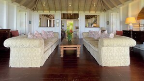 A spacious living room with two sofas facing each other, a wooden coffee table, and a ceiling fan. - Hermitage Nevis (Charlestown)
