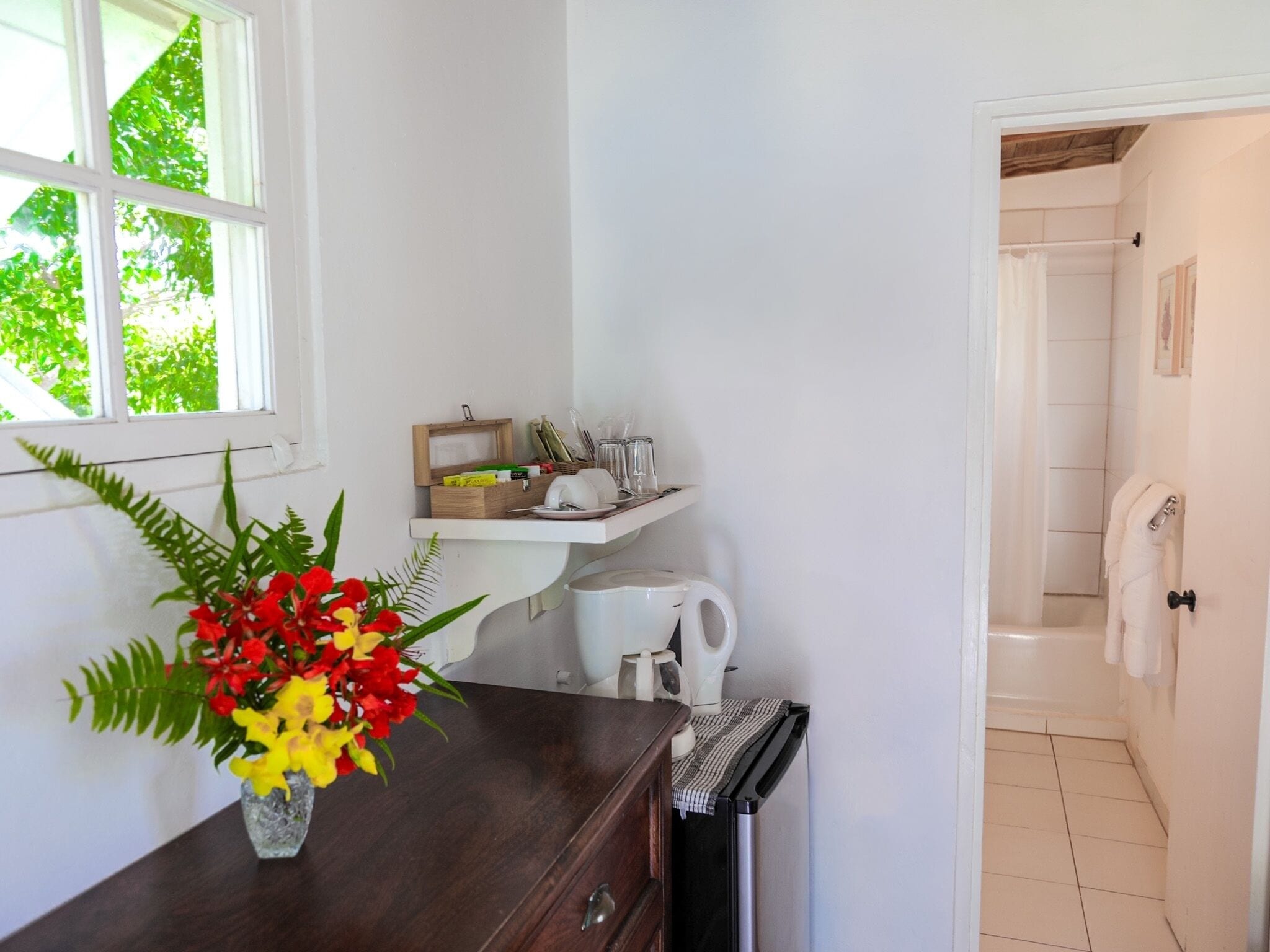 A bathroom with a white sink, a mirror, and a towel rack. There is a window with a view of green trees.