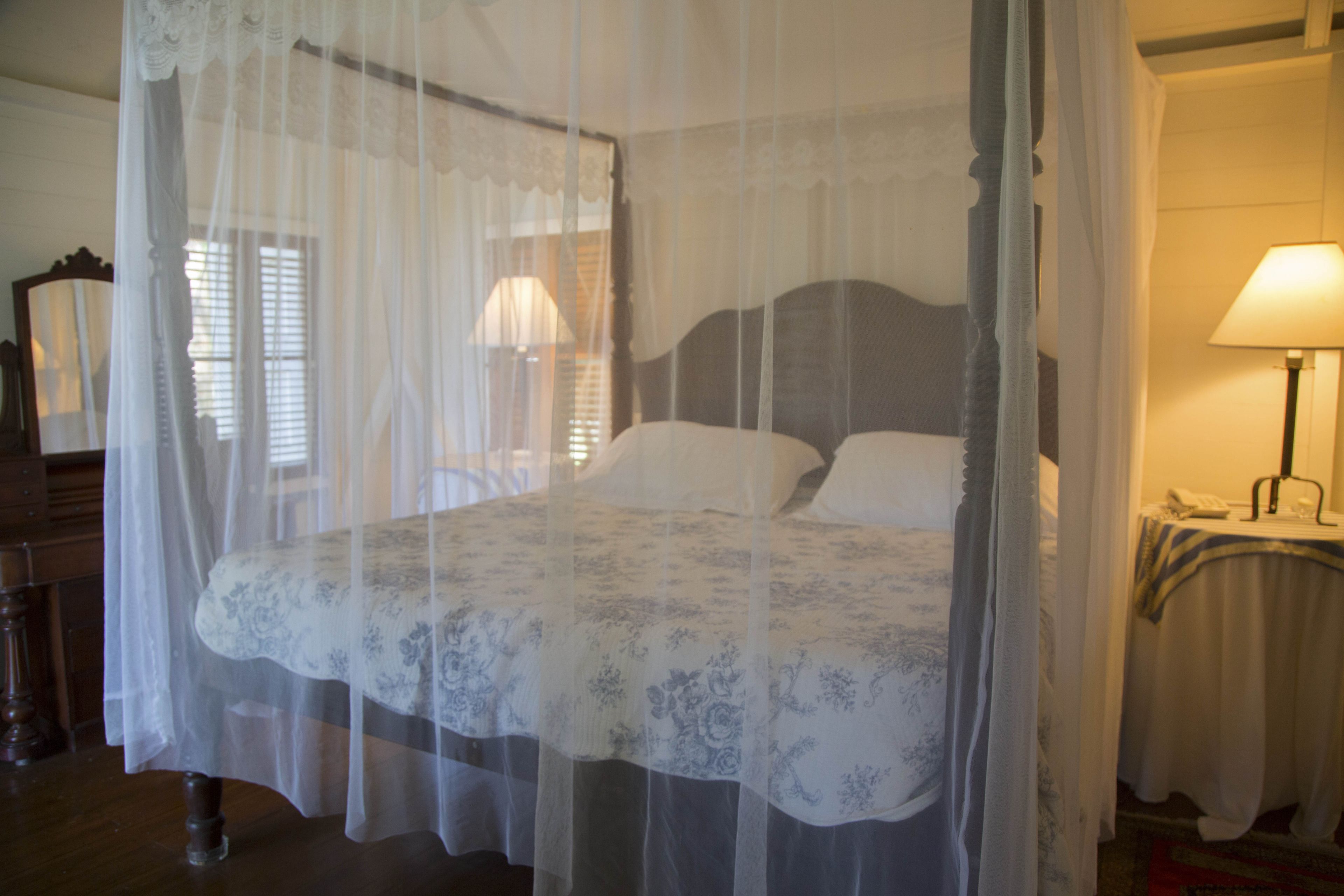 A bedroom with a canopy bed, a bedside table with a lamp, and a window with blinds.