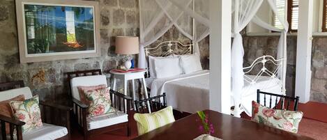A room with a stone wall, a bed with a canopy, a dining table with chairs, and a painting on the wall.