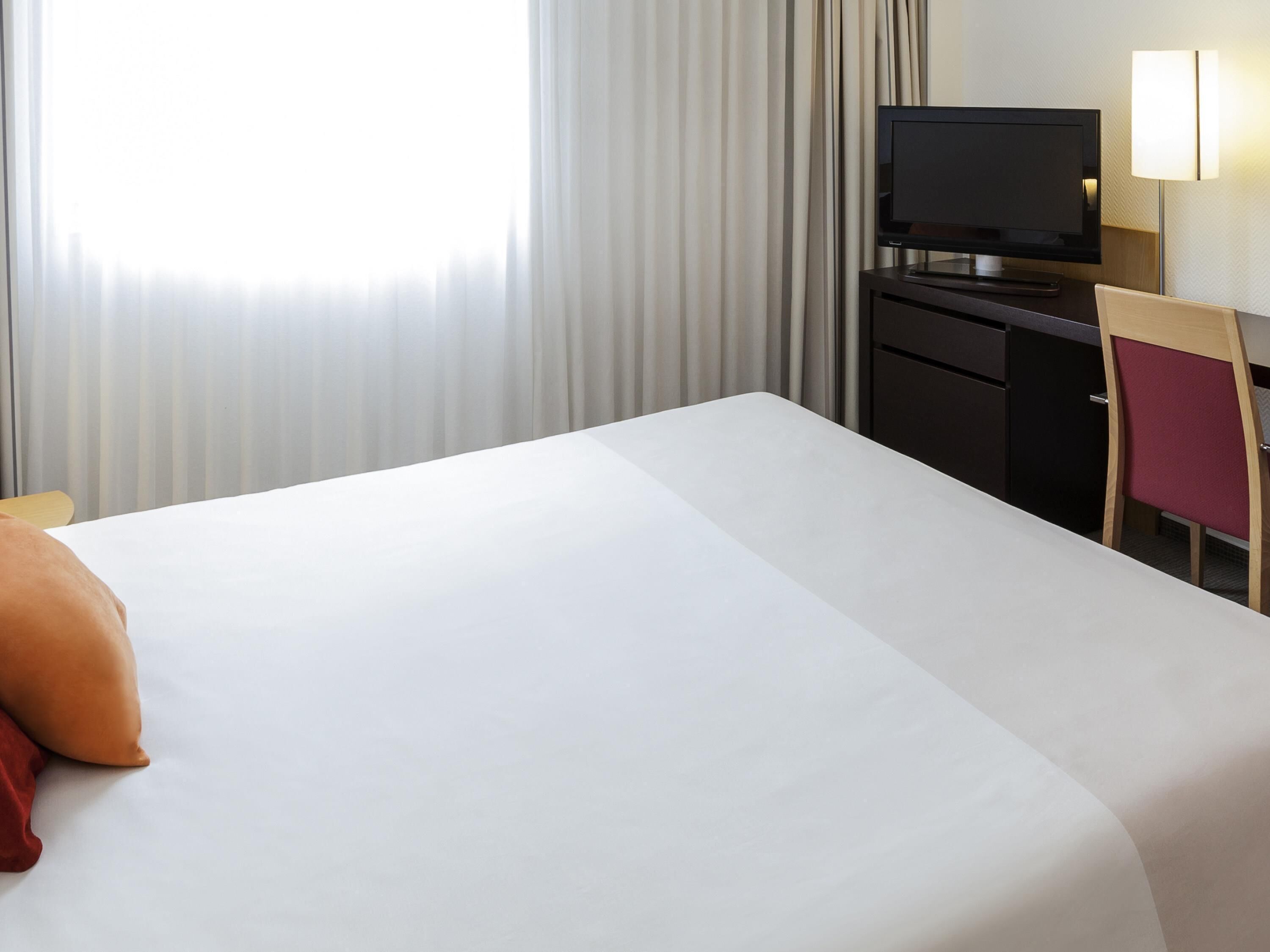 Ein Hotelzimmer mit Bett, Schreibtisch mit Fernseher, Stuhl und Lampe.