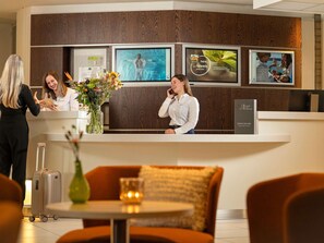 A hotel reception desk with framed artwork, a reception counter, and a seating area with a table and chairs. - Novotel Maastricht (Maastricht)