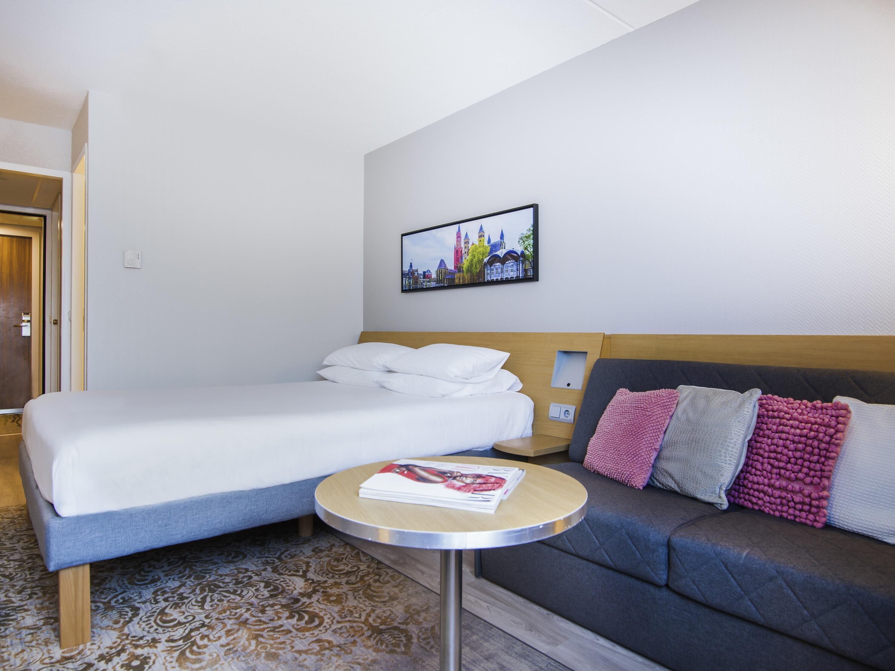 Une chambre d’hôtel avec un lit, un canapé, une petite table et un tableau accroché au mur.