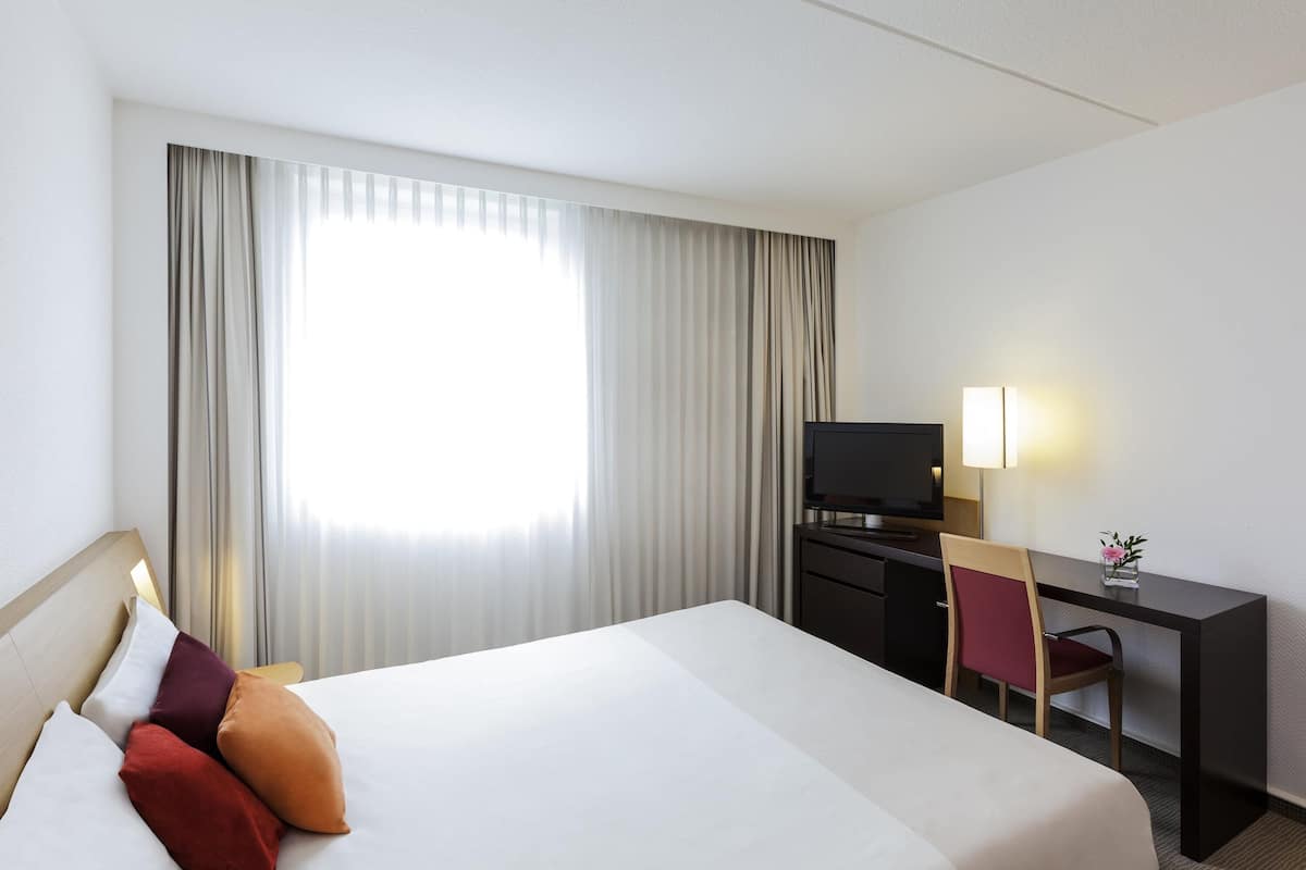 A hotel room with a bed, a desk, a television, and a lamp.