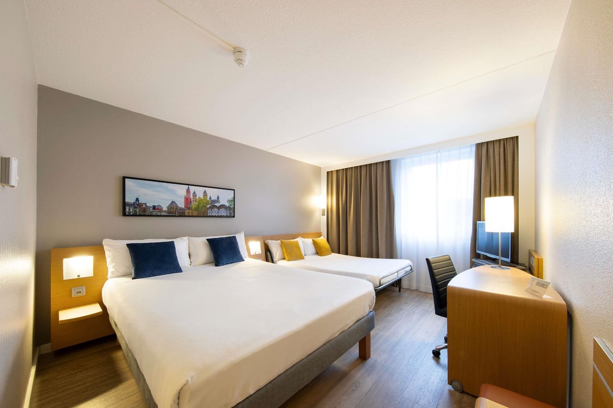 A hotel room with two beds, a desk, a chair, a TV, and a painting on the wall.
