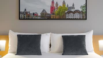 Habitación de hotel con cama, dos almohadas, una fotografía enmarcada de un paisaje urbano y cabecera de madera.