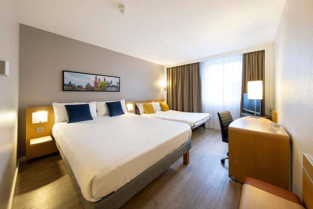 A hotel room with a large bed, a desk, a chair, a TV, and a painting on the wall.