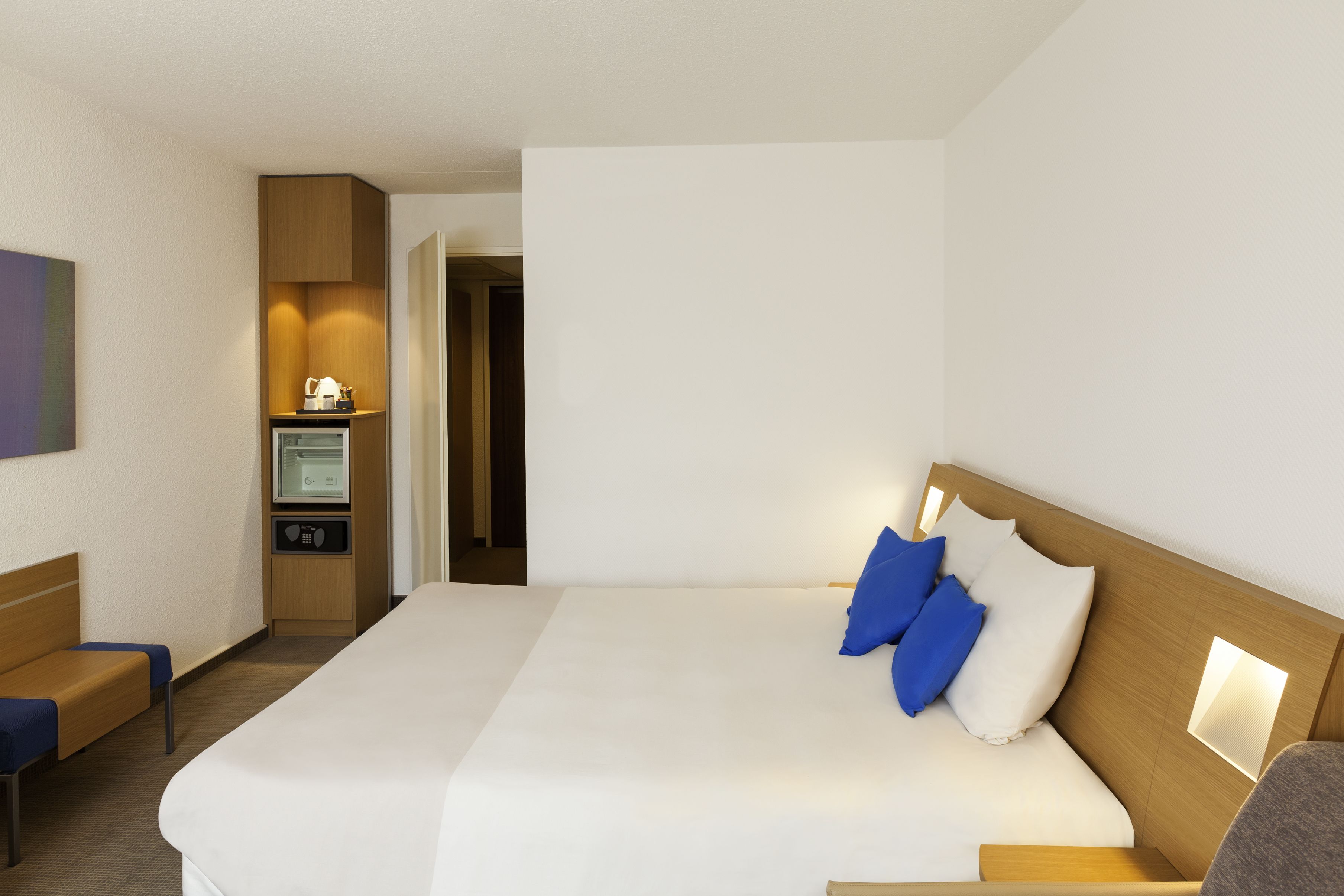 A hotel room with a large bed, a desk with a computer, and a small kitchenette.