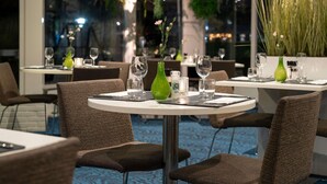 An indoor dining area with round tables, chairs, and potted plants. - Novotel Maastricht (Maastricht)