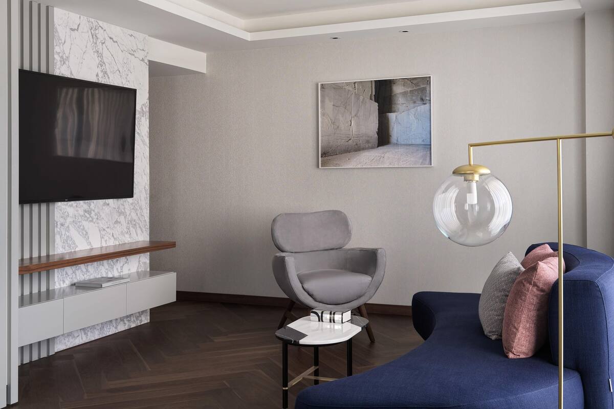 Un salon moderne avec un téléviseur à écran plat, un mur décoratif en marbre, un fauteuil gris, un canapé bleu et un lampadaire.