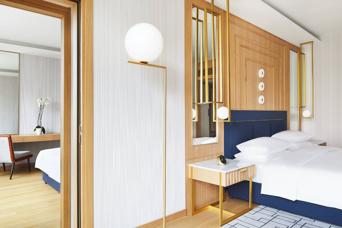 Une chambre d’hôtel moderne avec une tête de lit en bois, une table de chevet avec une lampe, un grand miroir et un bureau avec une chaise.