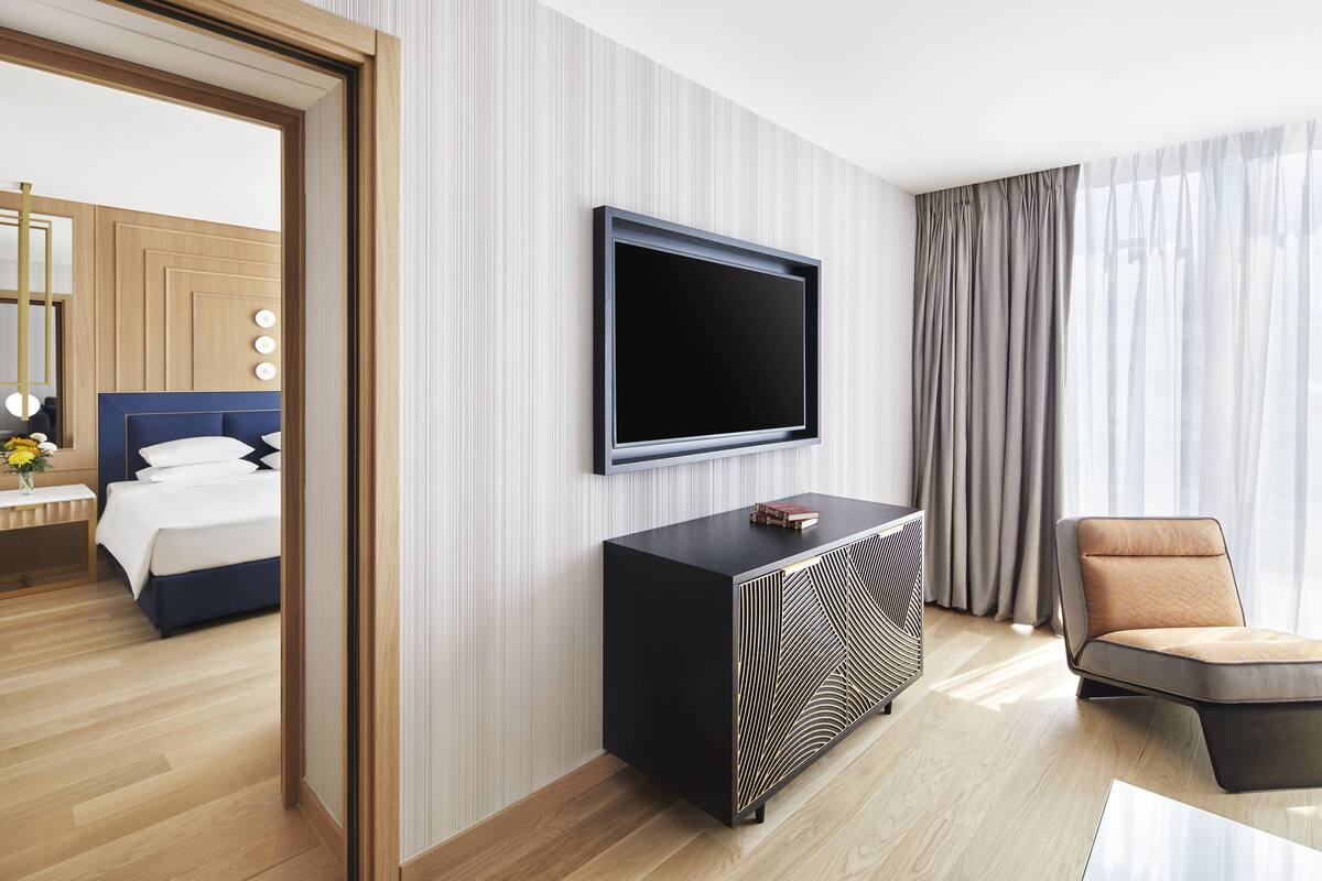 Une chambre d’hôtel moderne dotée d’un grand téléviseur à écran plat fixé au mur, d’une console noire au motif original, d’un fauteuil confortable et d’un lit bien fait avec une tête de lit bleue.