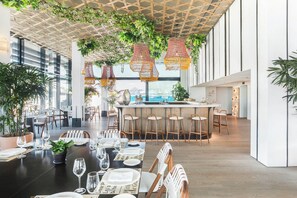 Une salle à manger spacieuse avec de hauts plafonds, des plantes suspendues et une vue sur la mer.