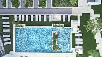 An aerial view of a modern hotel with a rectangular swimming pool surrounded by lounge chairs and greenery.